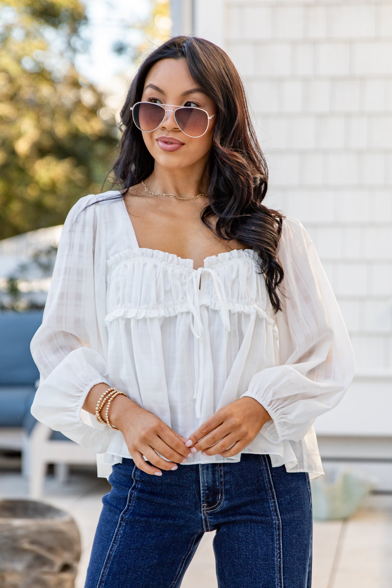 Woman wearing a white blouse and blue jeans outdoors.