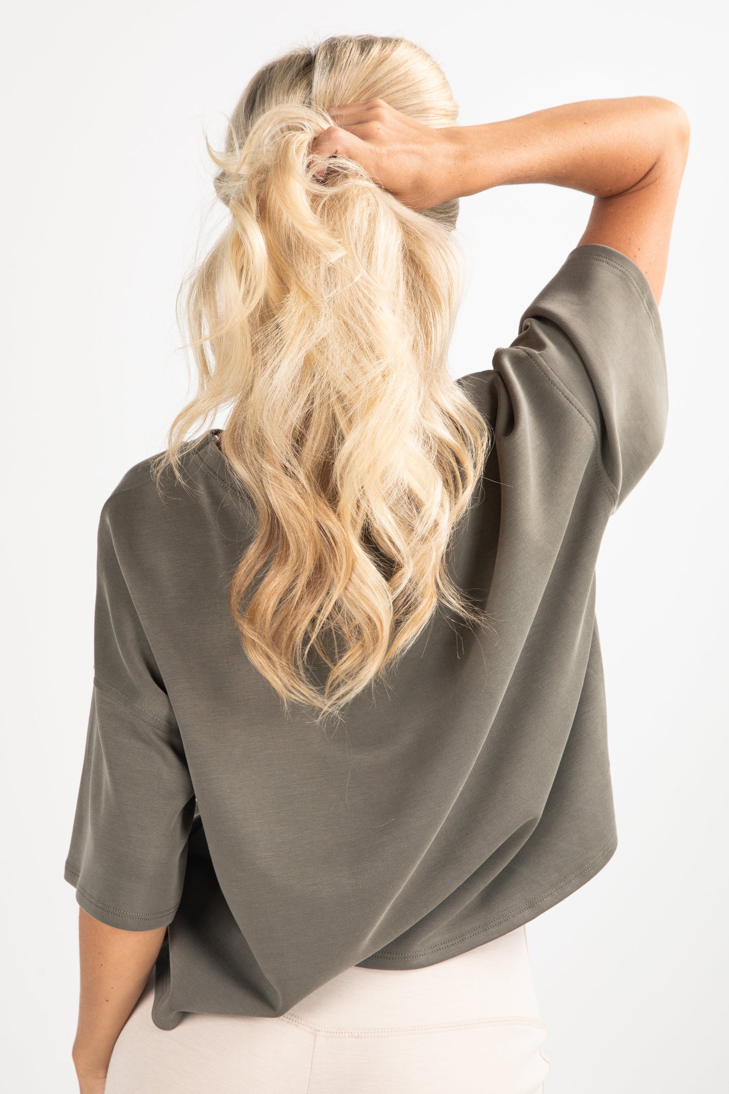 Person wearing a green shirt with long blonde hair styled in a ponytail against a white background