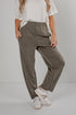 A person wearing loose, wide-leg olive green pants with an elastic waistband, styled with a white t-shirt and white sneakers against a plain light gray studio background.