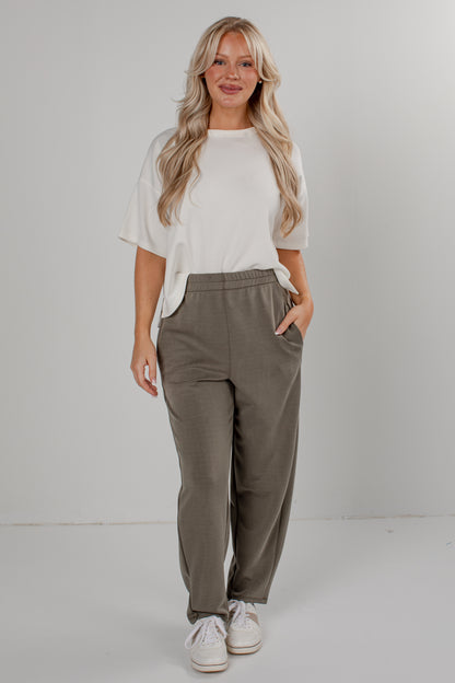 A woman modeling a white short-sleeve t-shirt and olive green wide-leg sweatpants, standing against a light gray studio background.
