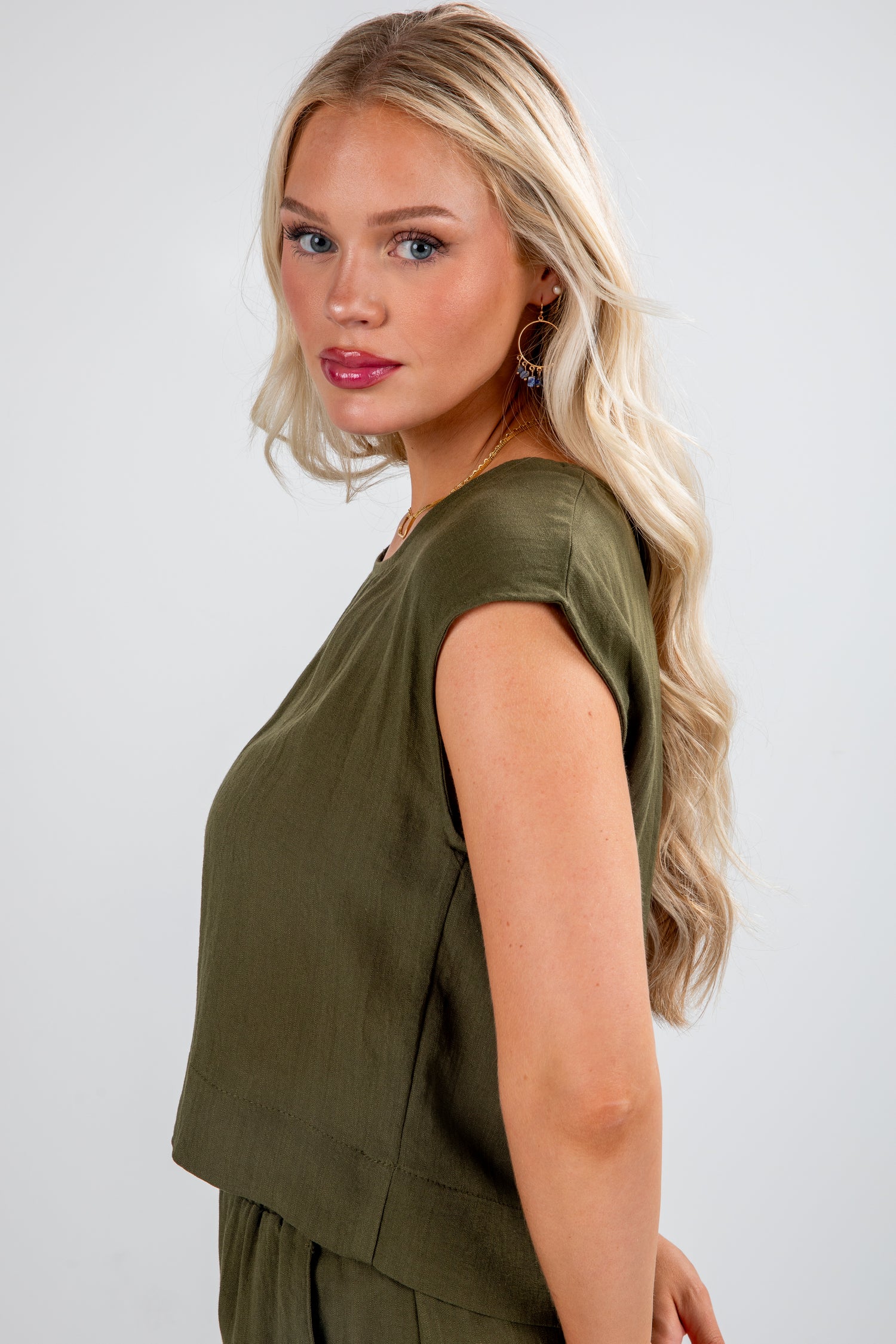 Woman wearing an olive green sleeveless top against a white background