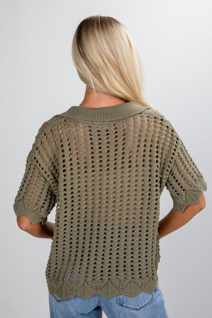 Person wearing a green knitted sweater on a plain background