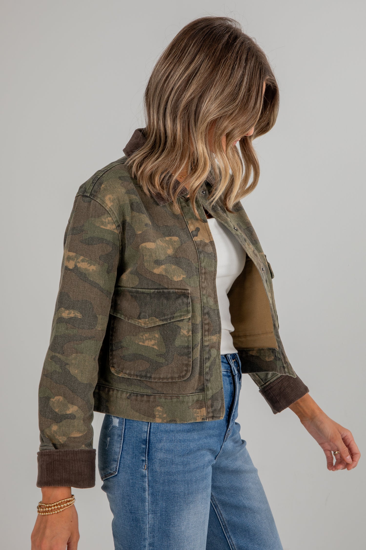 Person wearing a camouflage jacket and blue jeans on a plain background