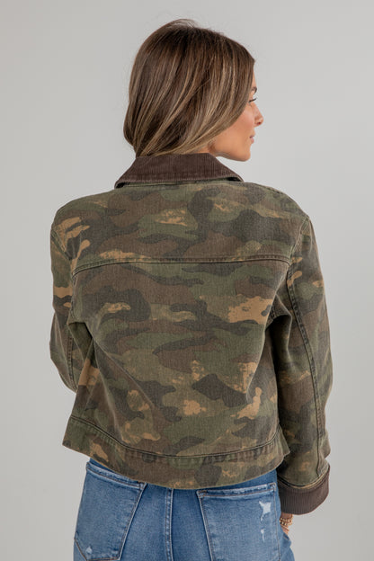 Person wearing a camouflage jacket and blue jeans on a gray background