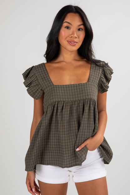 Woman wearing a green checkered top with ruffled sleeves on a white background