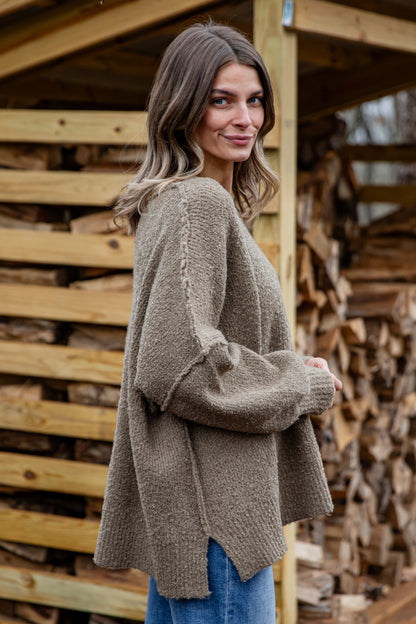 Woman wearing a brown sweater standing in front of stacked firewood.