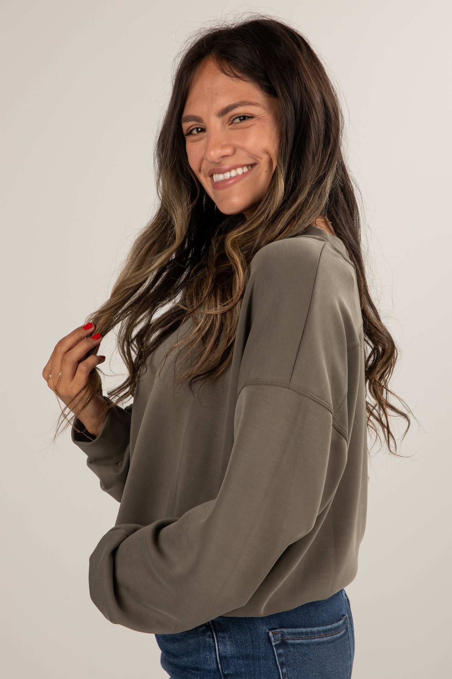 Woman wearing a beige sweater and blue jeans against a plain background