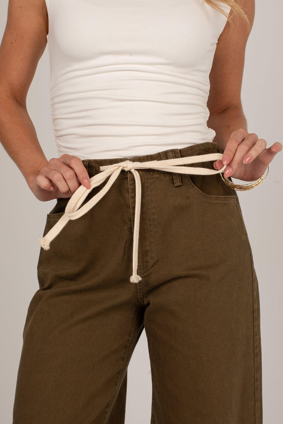 A close-up of a person wearing olive green wide-leg pants with an off-white drawstring belt tied at the waist, paired with a white ribbed tank top.