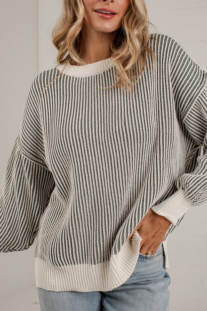 A woman wearing an oversized knit sweater with vertical gray and off-white stripes, paired with light blue jeans.