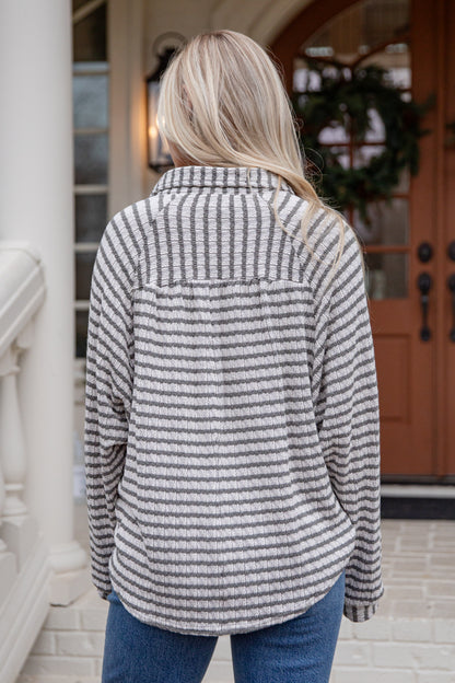 Person wearing a striped shirt standing in front of a door with a wreath.