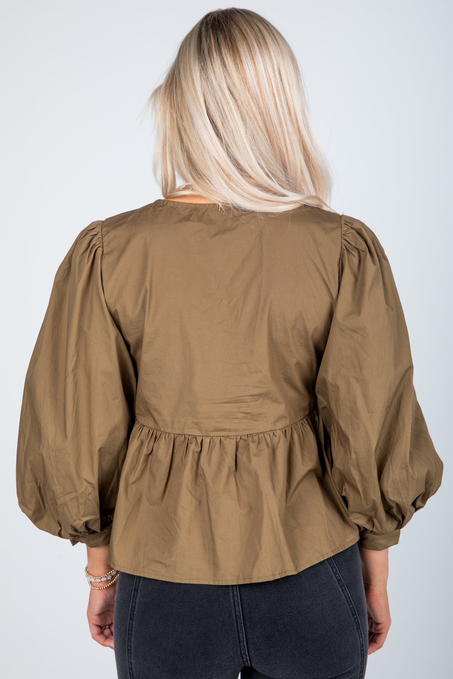 Person wearing a brown blouse with puffed sleeves on a white background