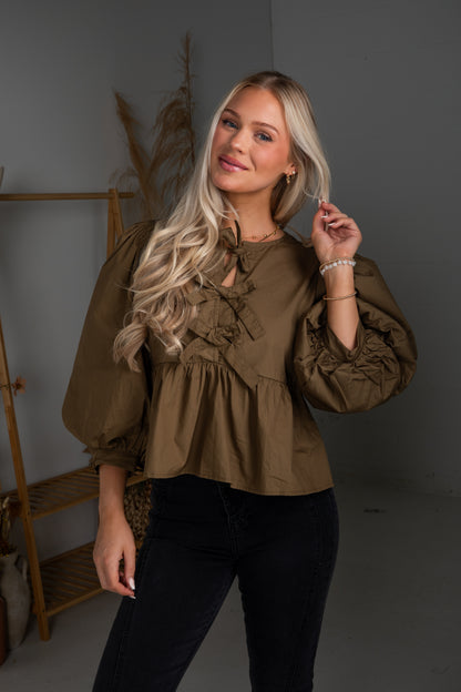 Woman wearing a brown blouse with ruffled details against a neutral background