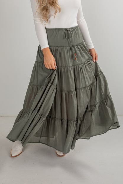 Person wearing a long, tiered olive green skirt on a plain background