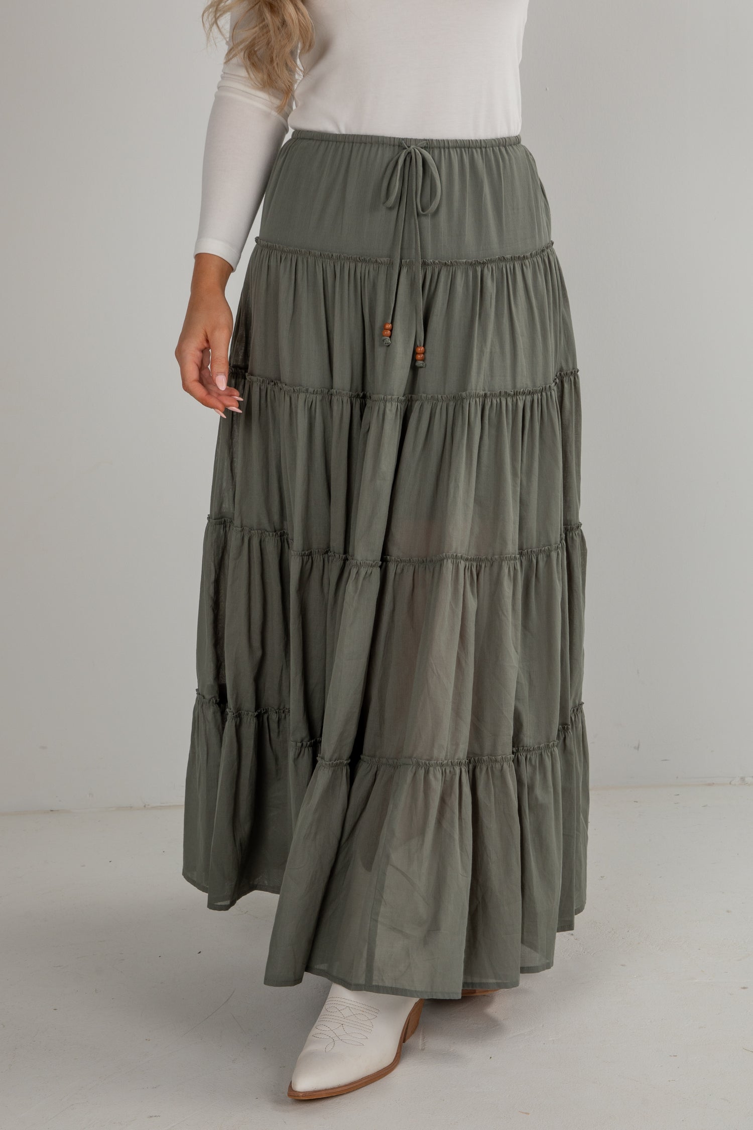 Woman wearing a long, tiered olive green skirt on a white background