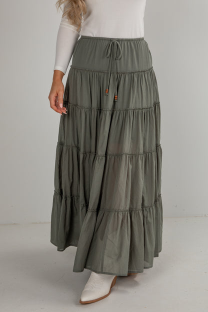 Woman wearing a long, tiered olive green skirt on a white background