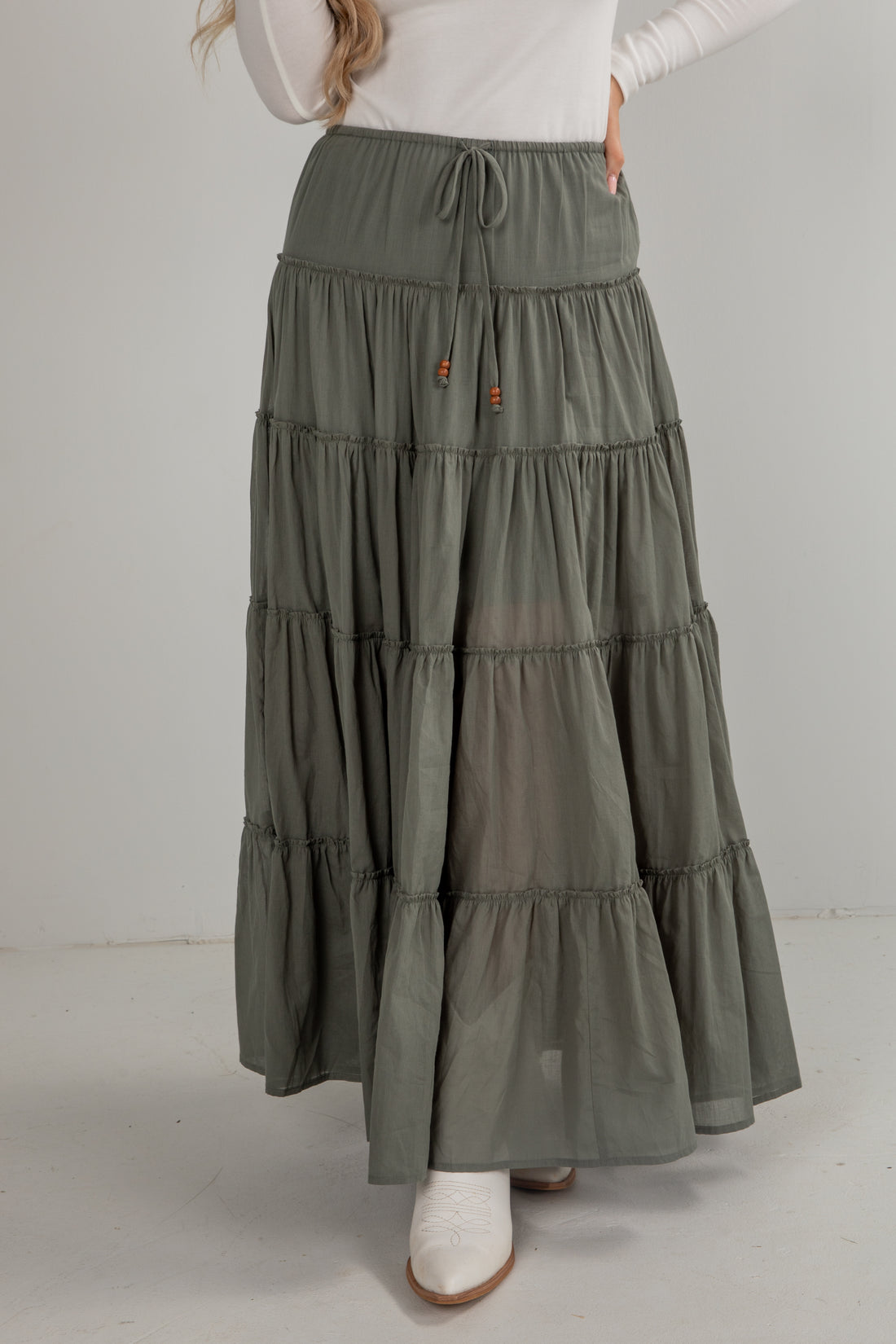 Person wearing a long, tiered olive green skirt on a plain background