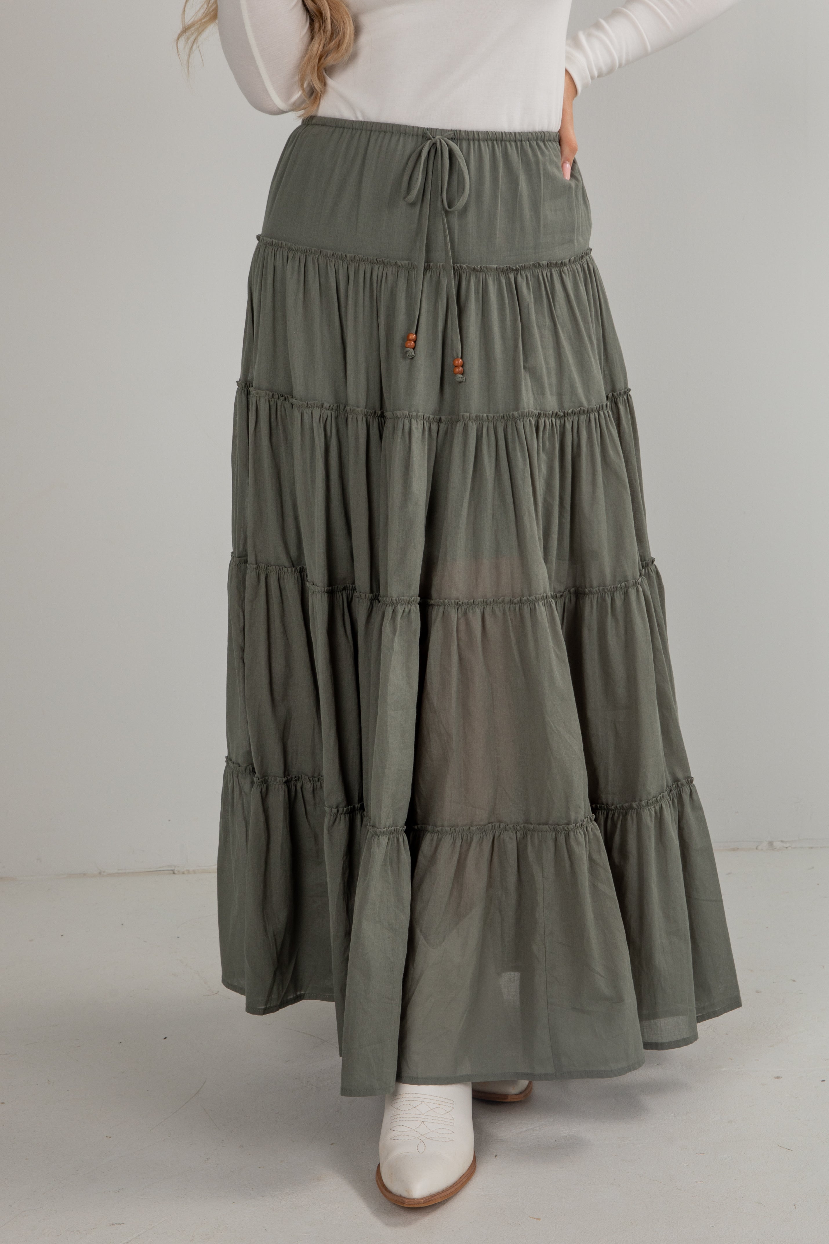 Person wearing a long, tiered olive green skirt on a plain background