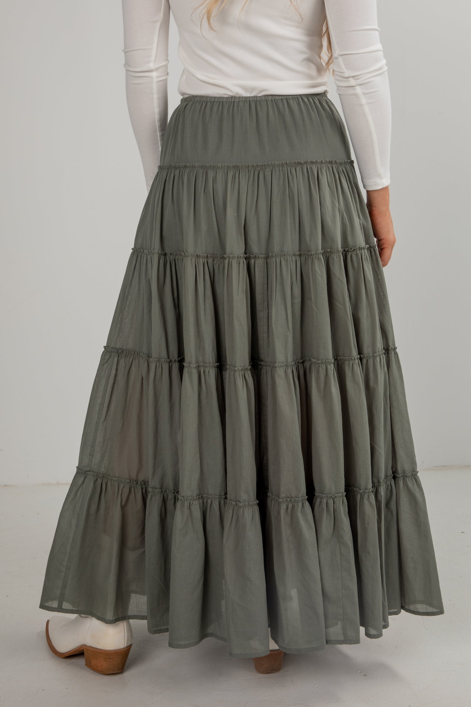 Person wearing a long, tiered green skirt with a white top on a plain background