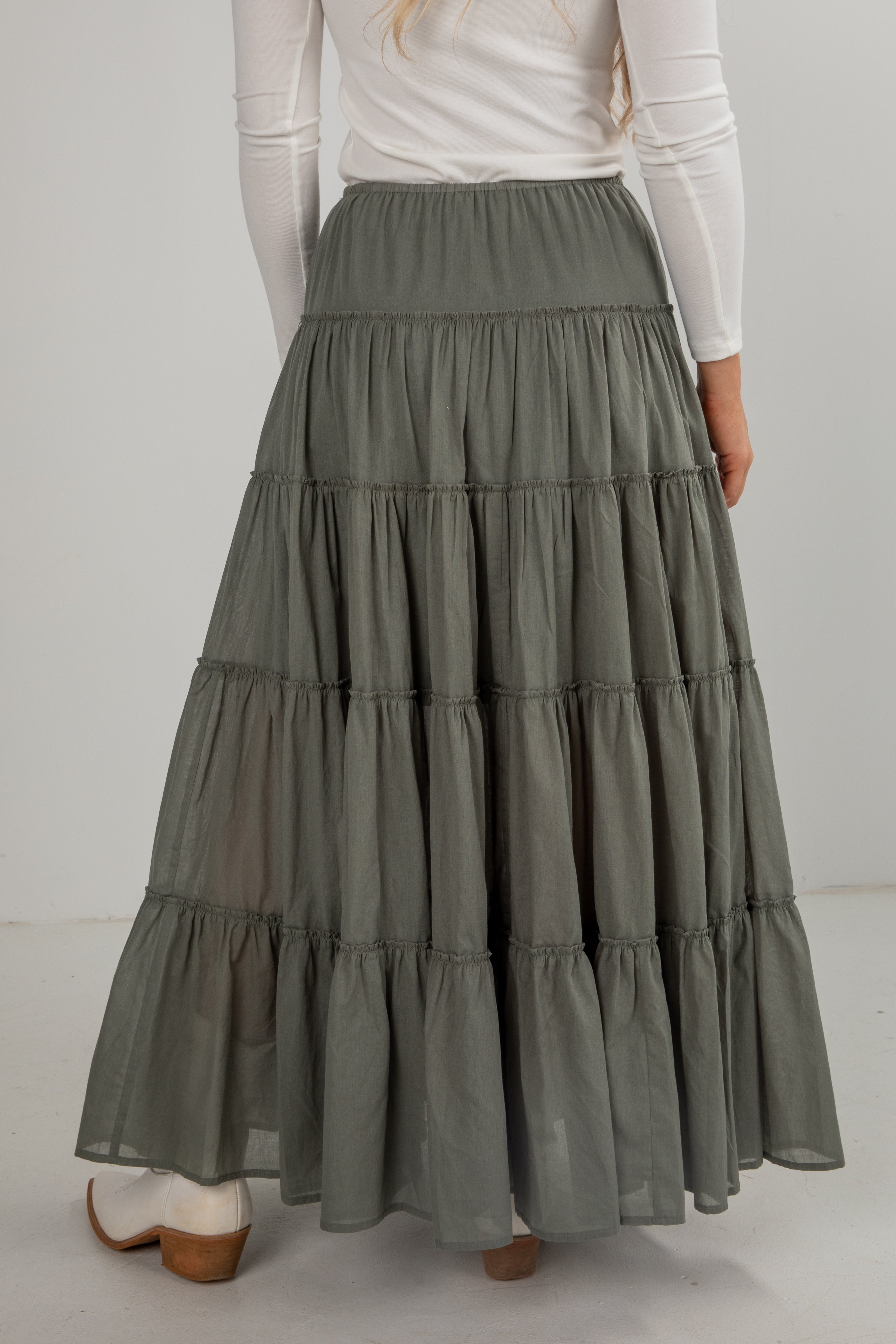 Person wearing a long, tiered green skirt with a white top on a plain background