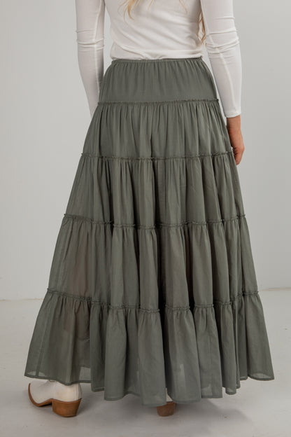 Person wearing a long, tiered green skirt with a white top on a plain background