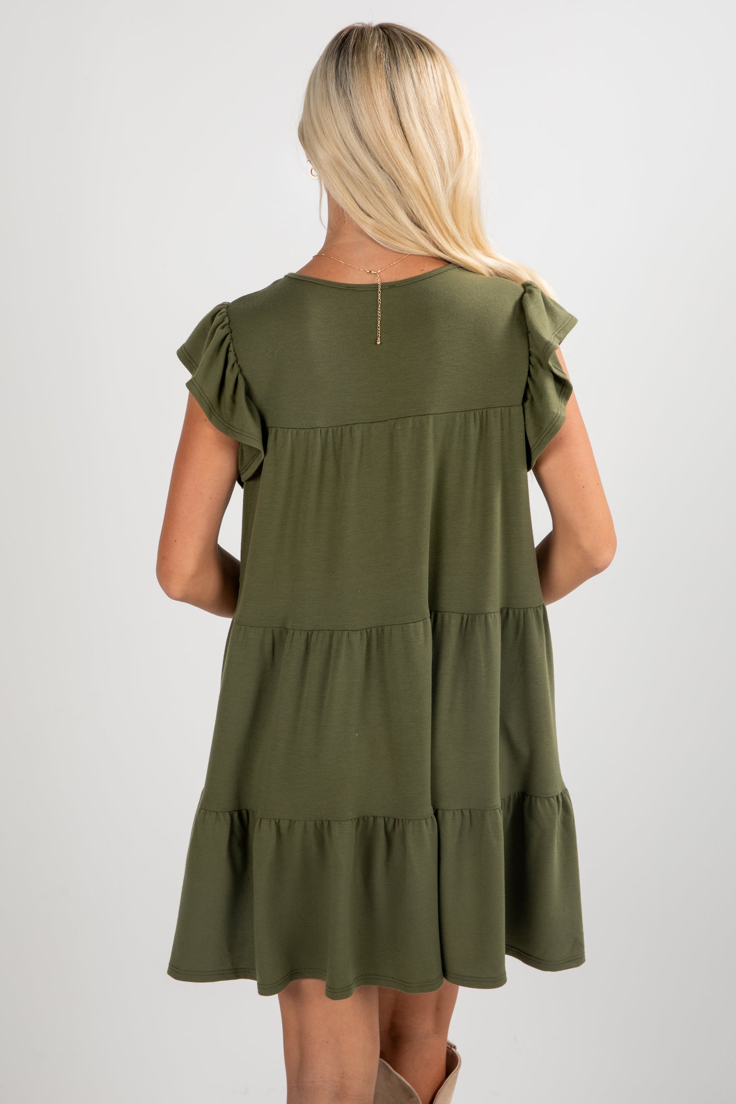 Woman wearing an olive green dress with ruffled sleeves on a white background