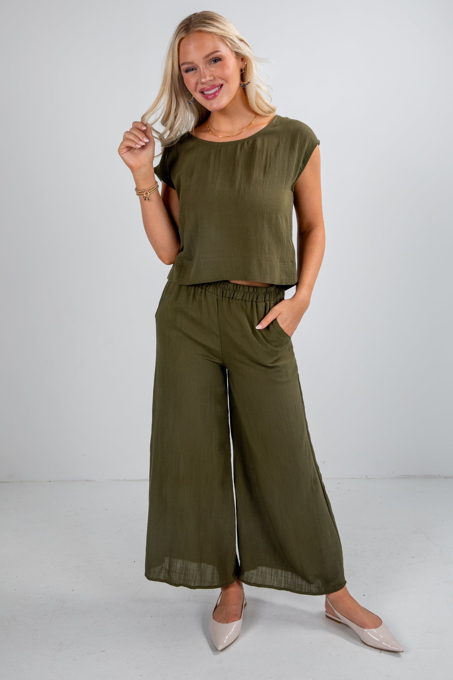 Woman wearing an olive green top and wide-leg pants on a white background