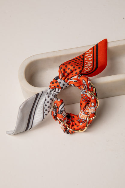 Orange patterned scrunchie with a matching scarf on a white surface
