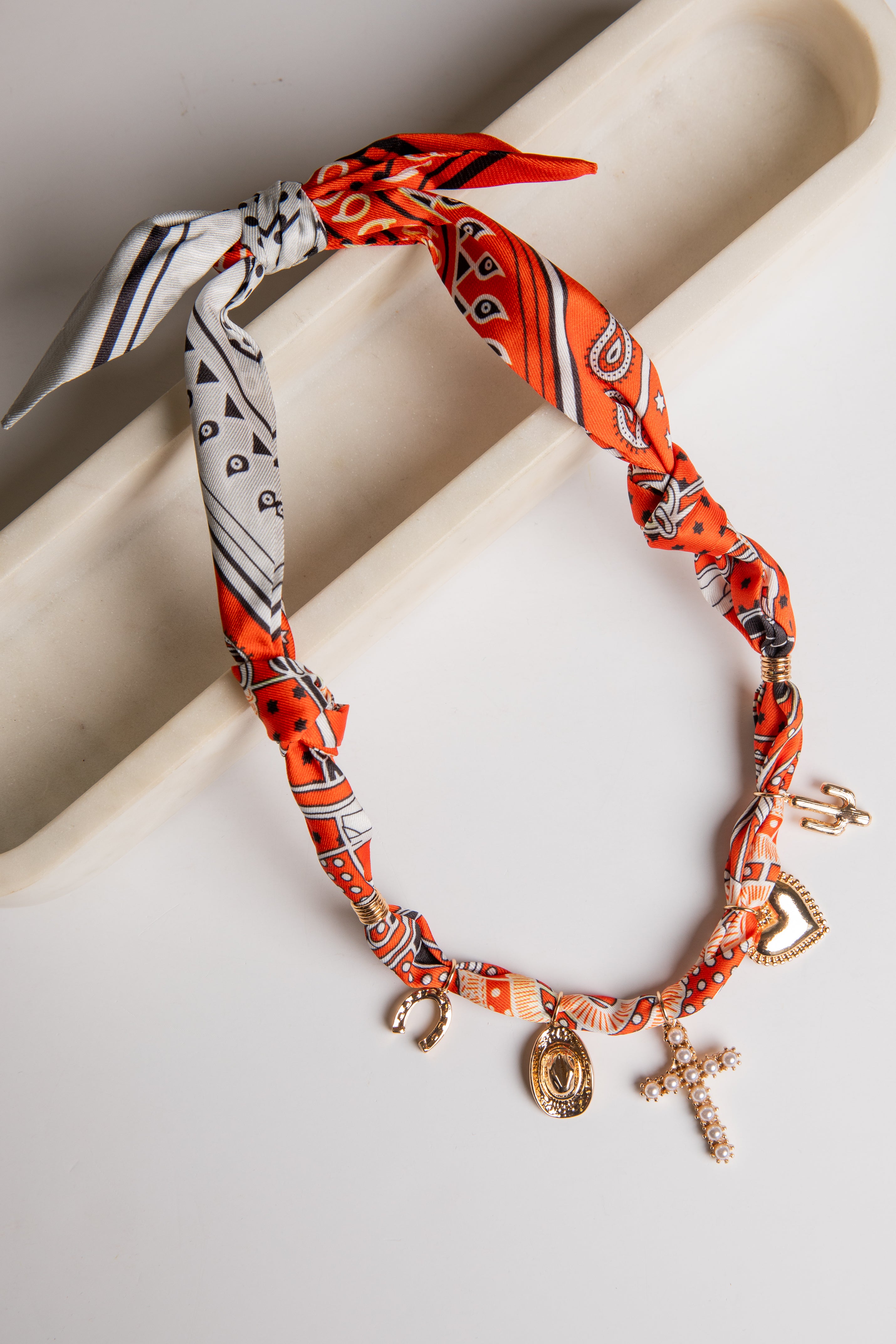 Bracelet with orange patterned bandana wrap and charms on a light background