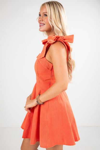 Woman wearing an orange dress with a bow detail on a white background