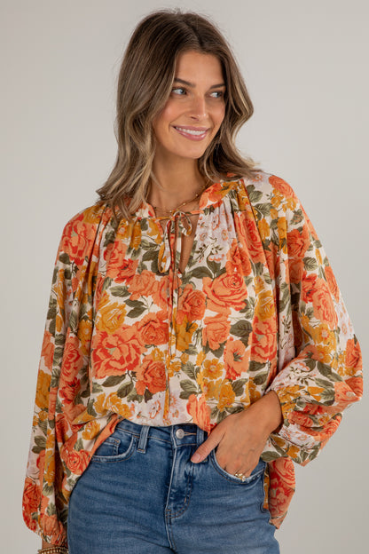 Woman wearing a floral blouse with long sleeves and blue jeans on a plain background