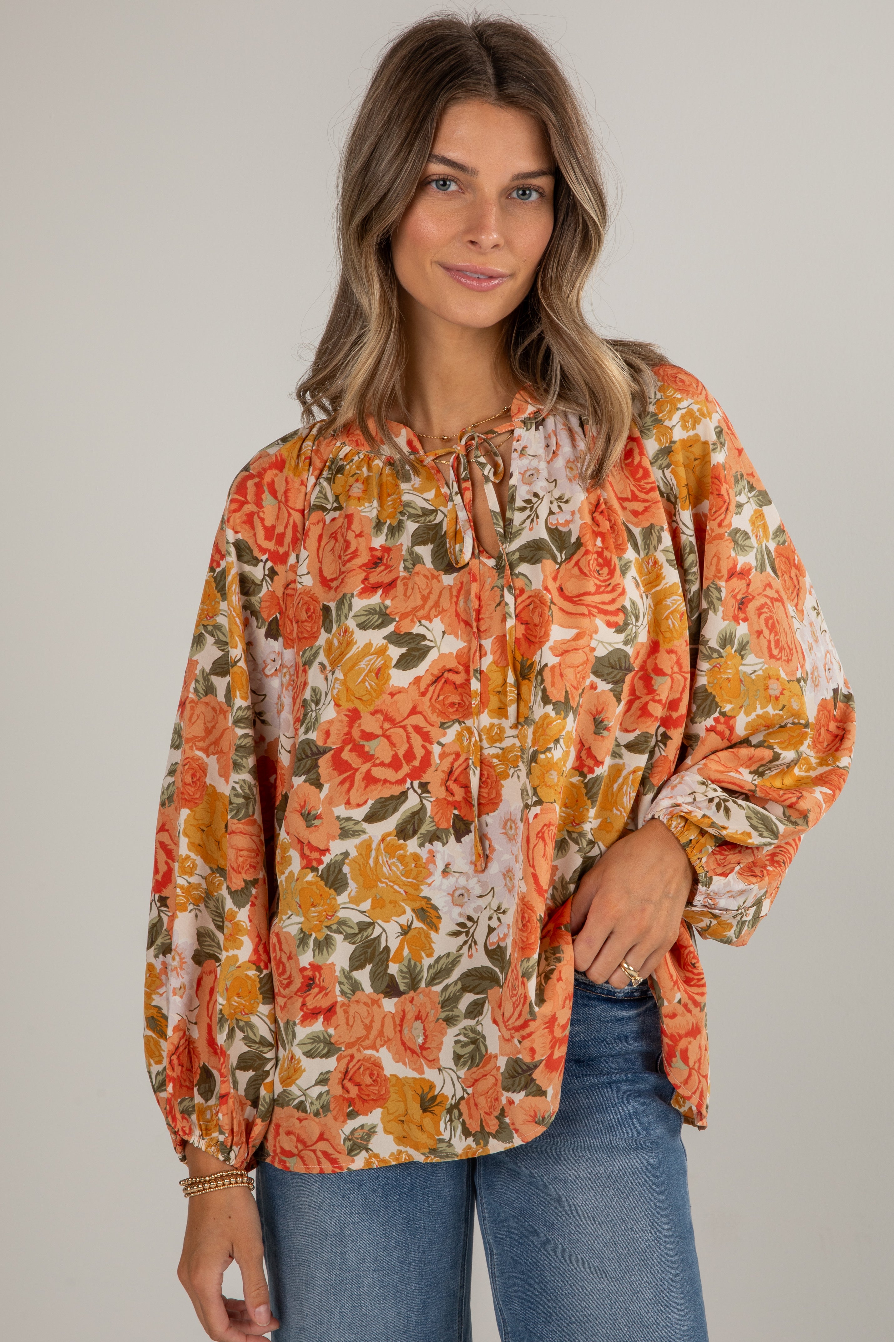Woman wearing a floral blouse with orange and green flowers on a plain background