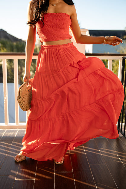 Woman wearing a coral dress standing on a balcony with a scenic background