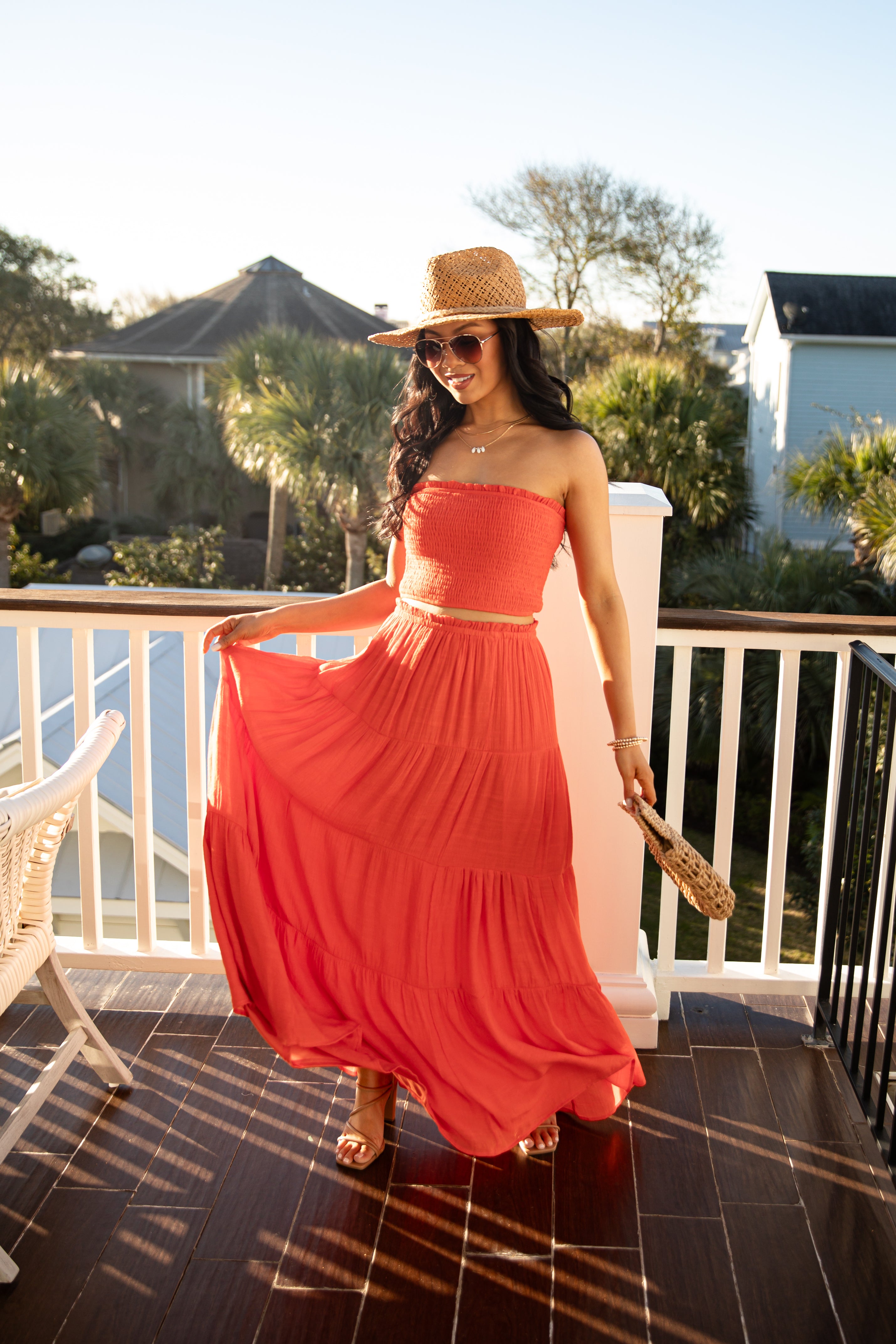 Woman in a red dress and straw hat standing on a balcony