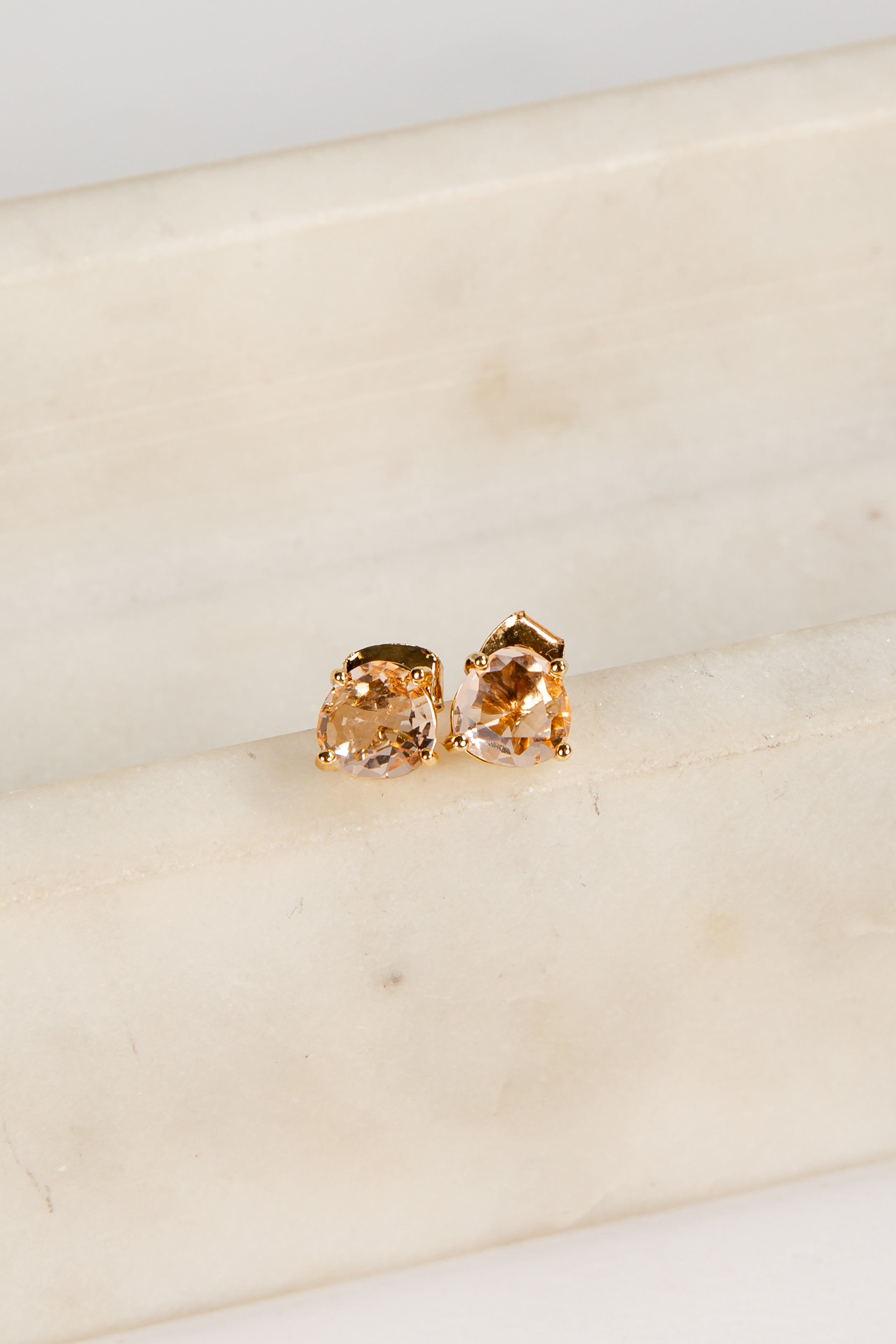 Gold earrings with orange gemstones on a light beige surface