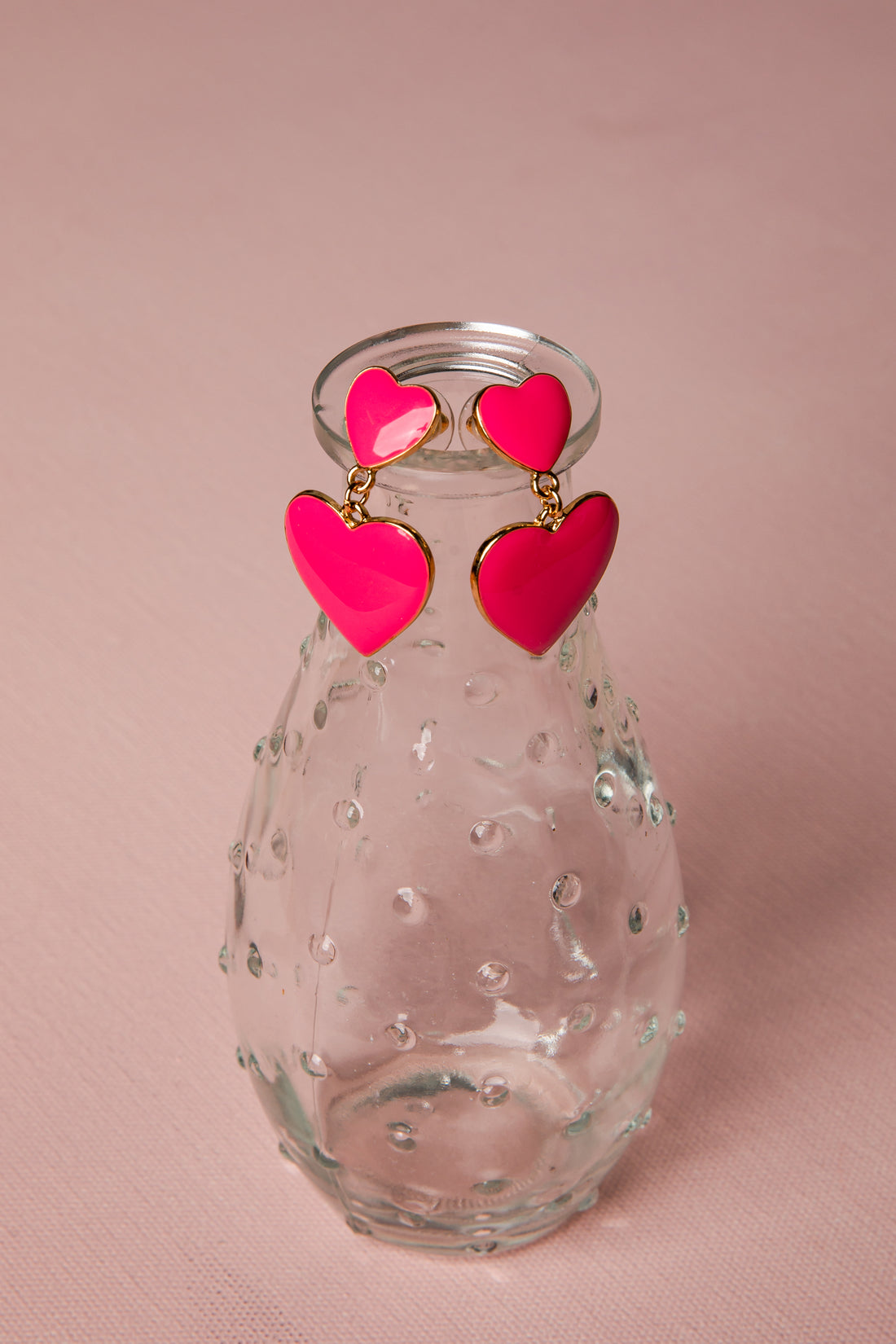 Clear glass vase with pink heart-shaped earrings on a pink background