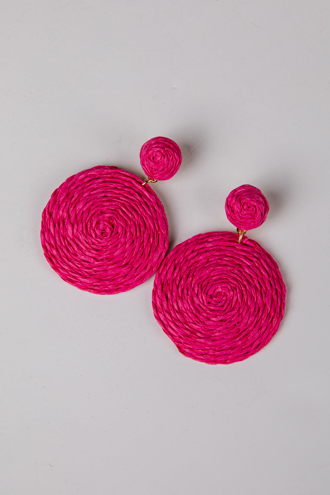 Pair of bright pink circular earrings on a light gray background