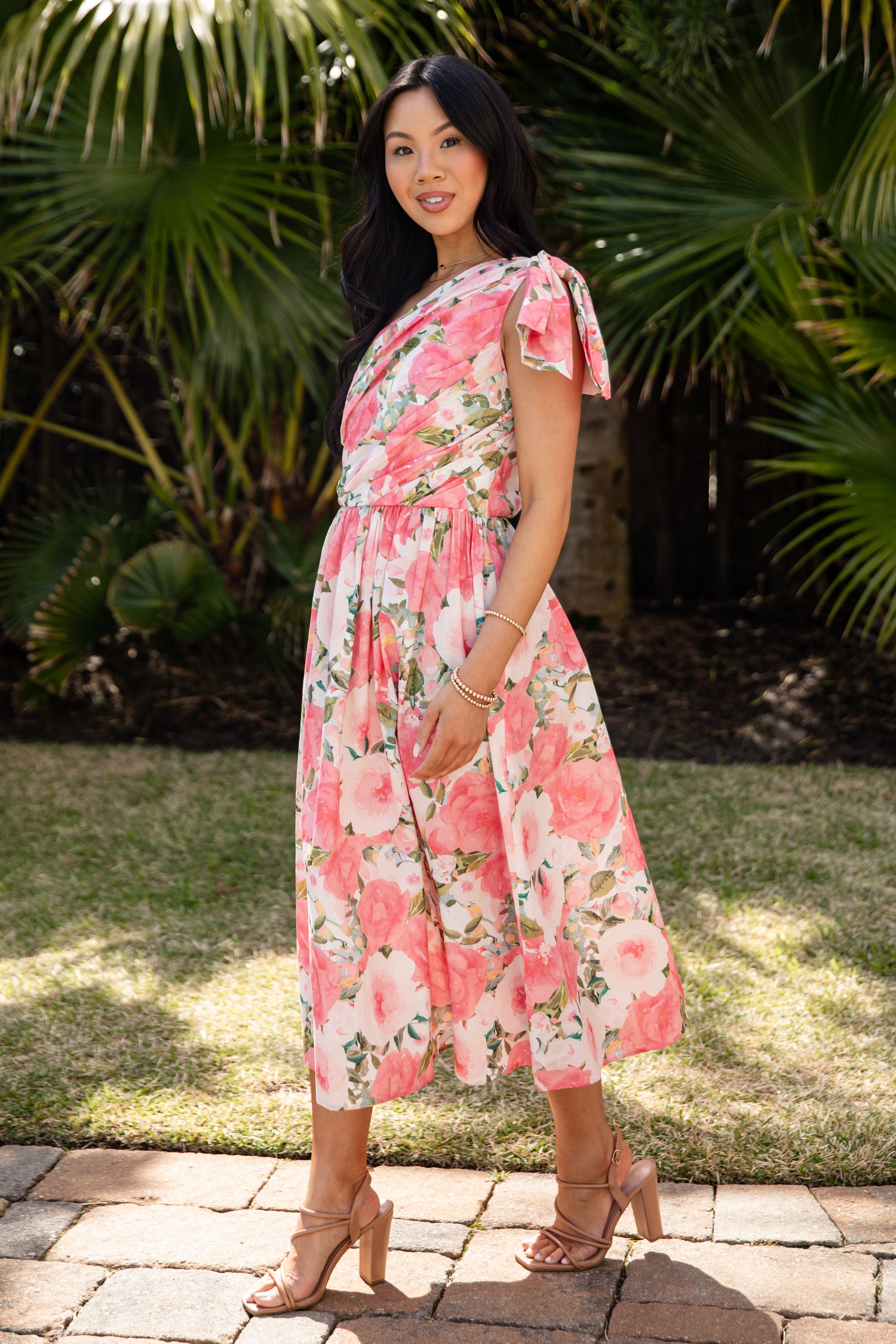 Woman wearing a floral dress standing outdoors with greenery in the background