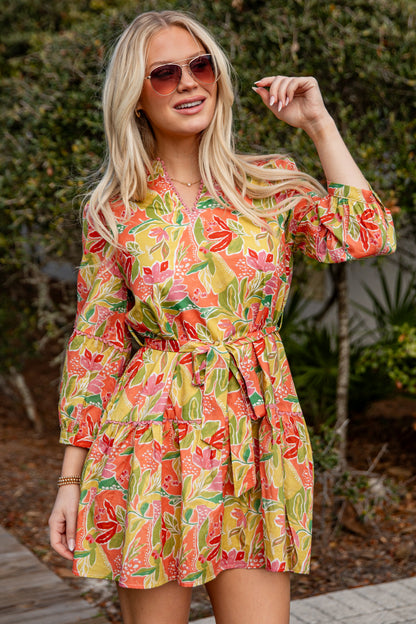 Woman wearing a colorful floral dress with sunglasses outdoors.