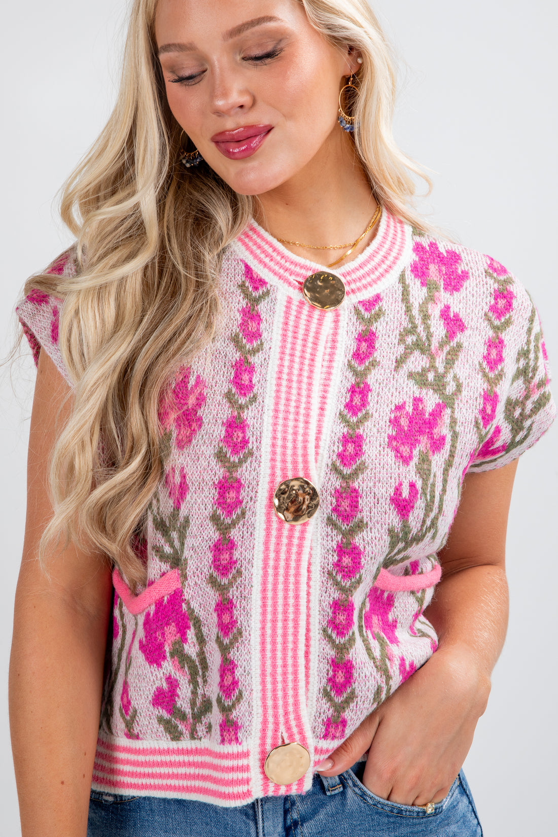Woman wearing a pink floral embroidered top with buttons on a white background