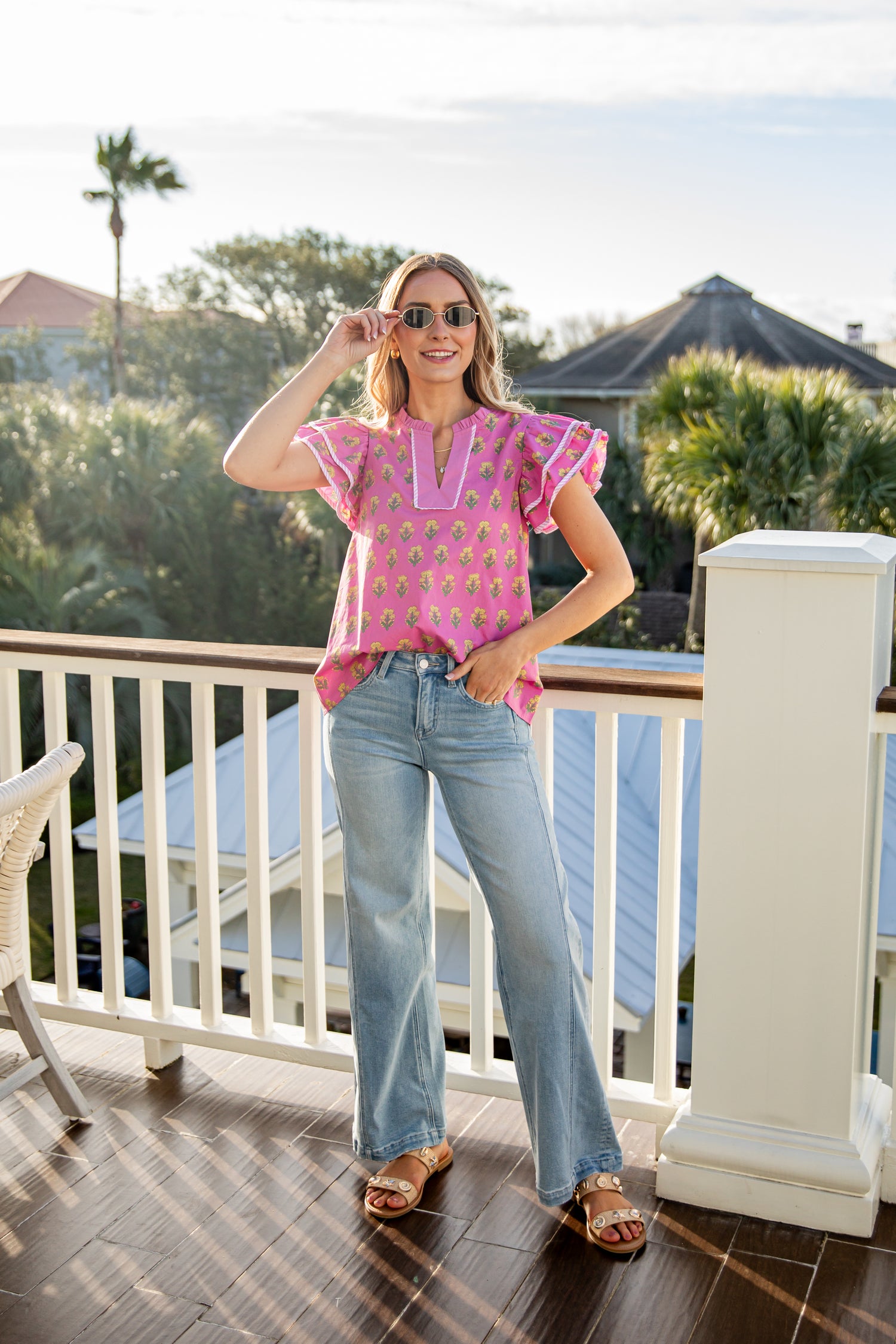 Woman in a pink top and blue jeans standing on a balcony with a scenic background