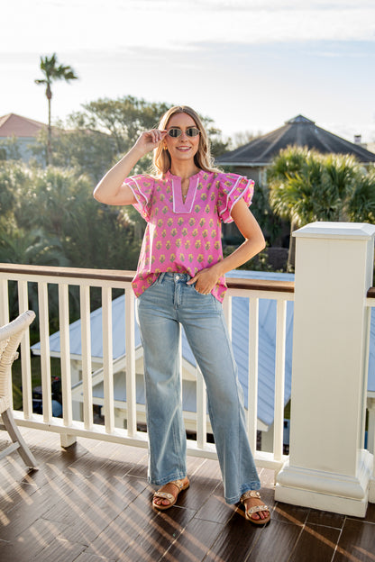 Woman in a pink top and blue jeans standing on a balcony with a scenic background
