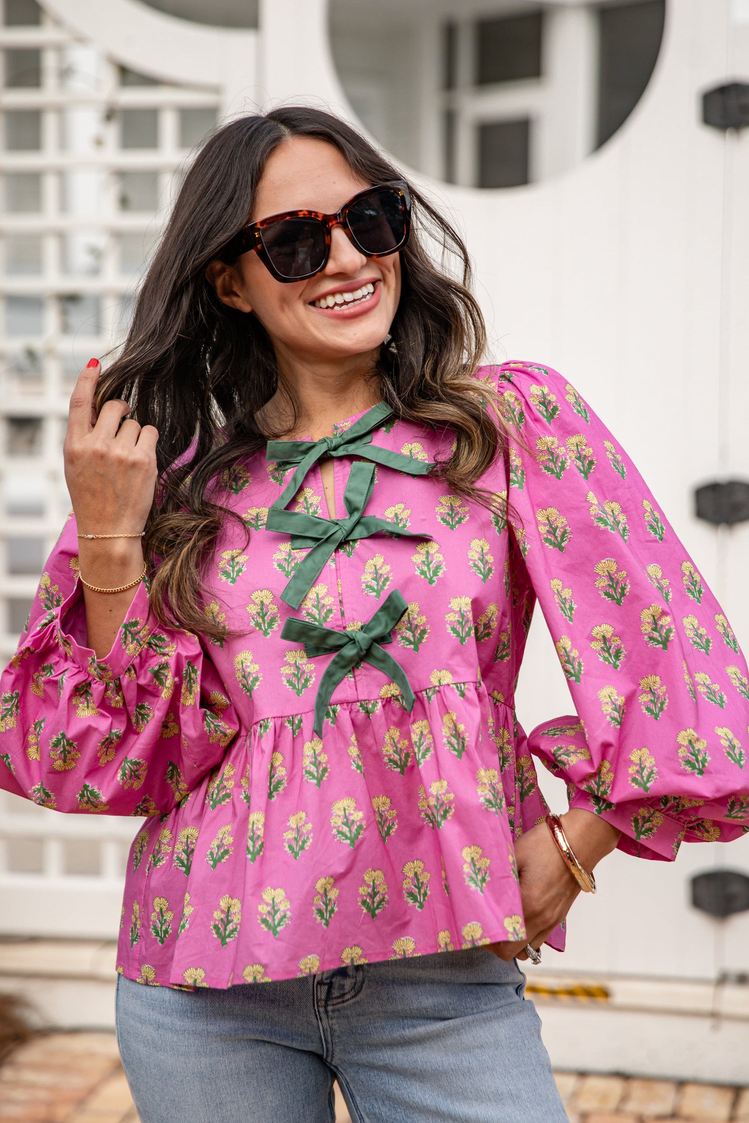 Woman wearing a pink floral blouse with green accents outdoors.