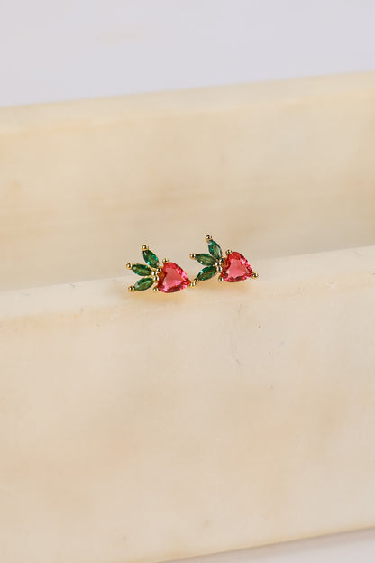 Heart-shaped earrings with green and red stones on a beige surface