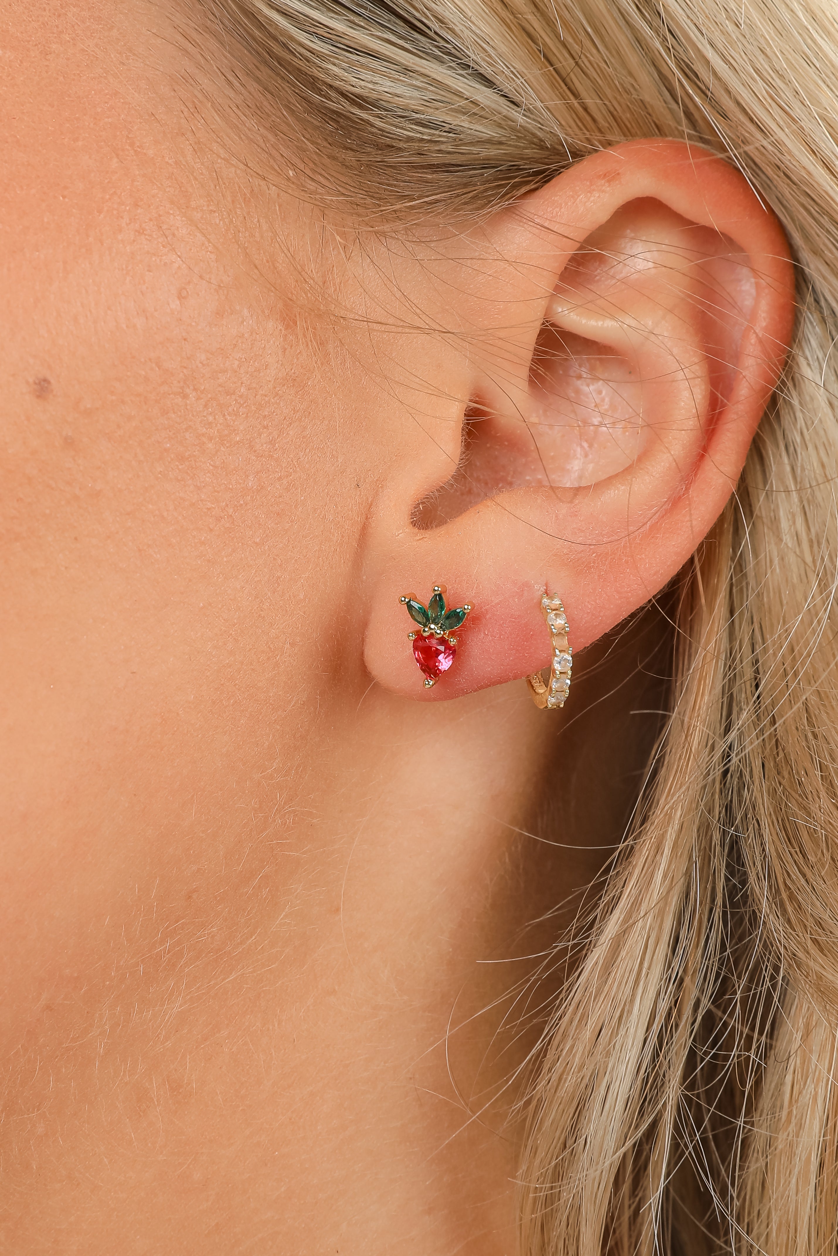 Close-up of an ear wearing a strawberry-shaped earring with a gold hoop.