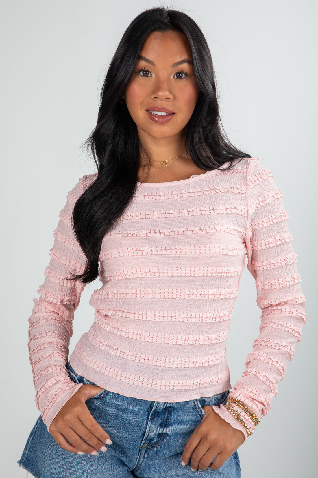 Woman wearing a pink textured sweater and blue jeans on a plain background