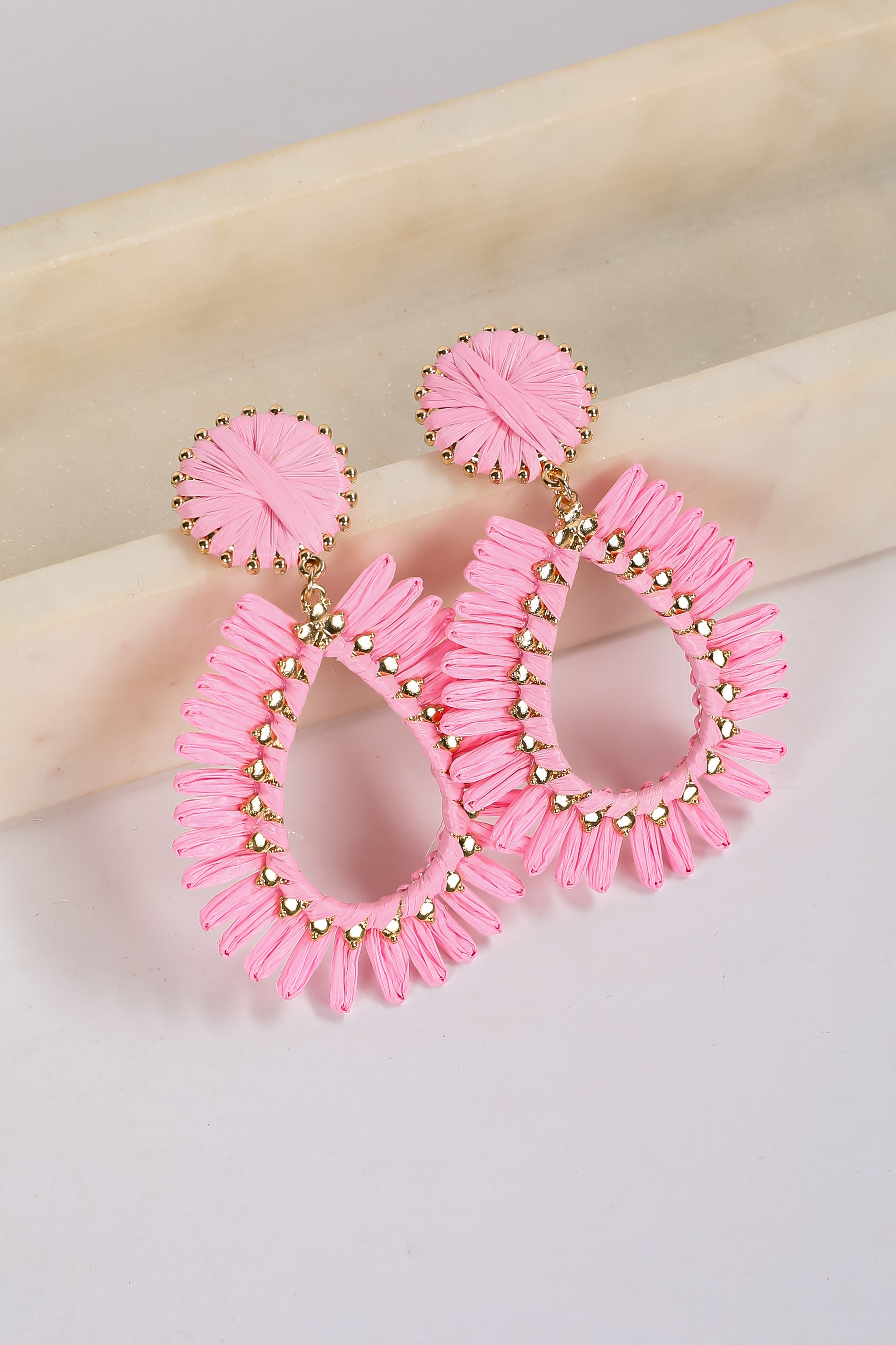 Pink hoop earrings with gold accents on a beige surface