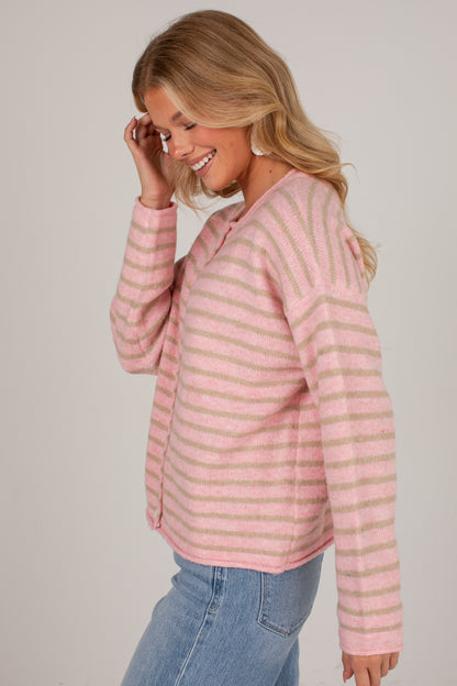 A woman wearing a pink and beige striped knit sweater with blue jeans, shown from a side profile against a light gray studio background.