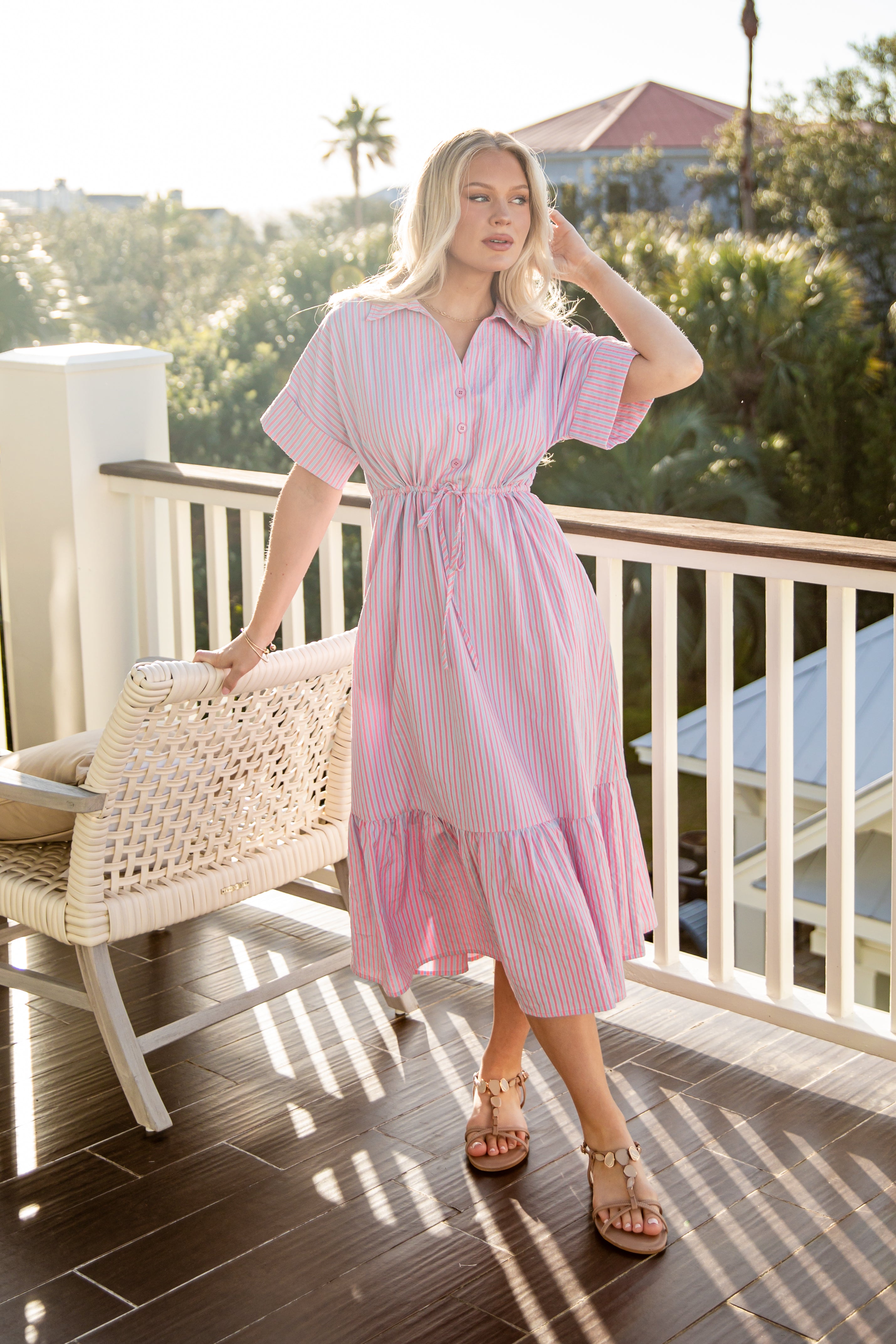 Woman in a pink dress standing on a balcony with greenery in the background