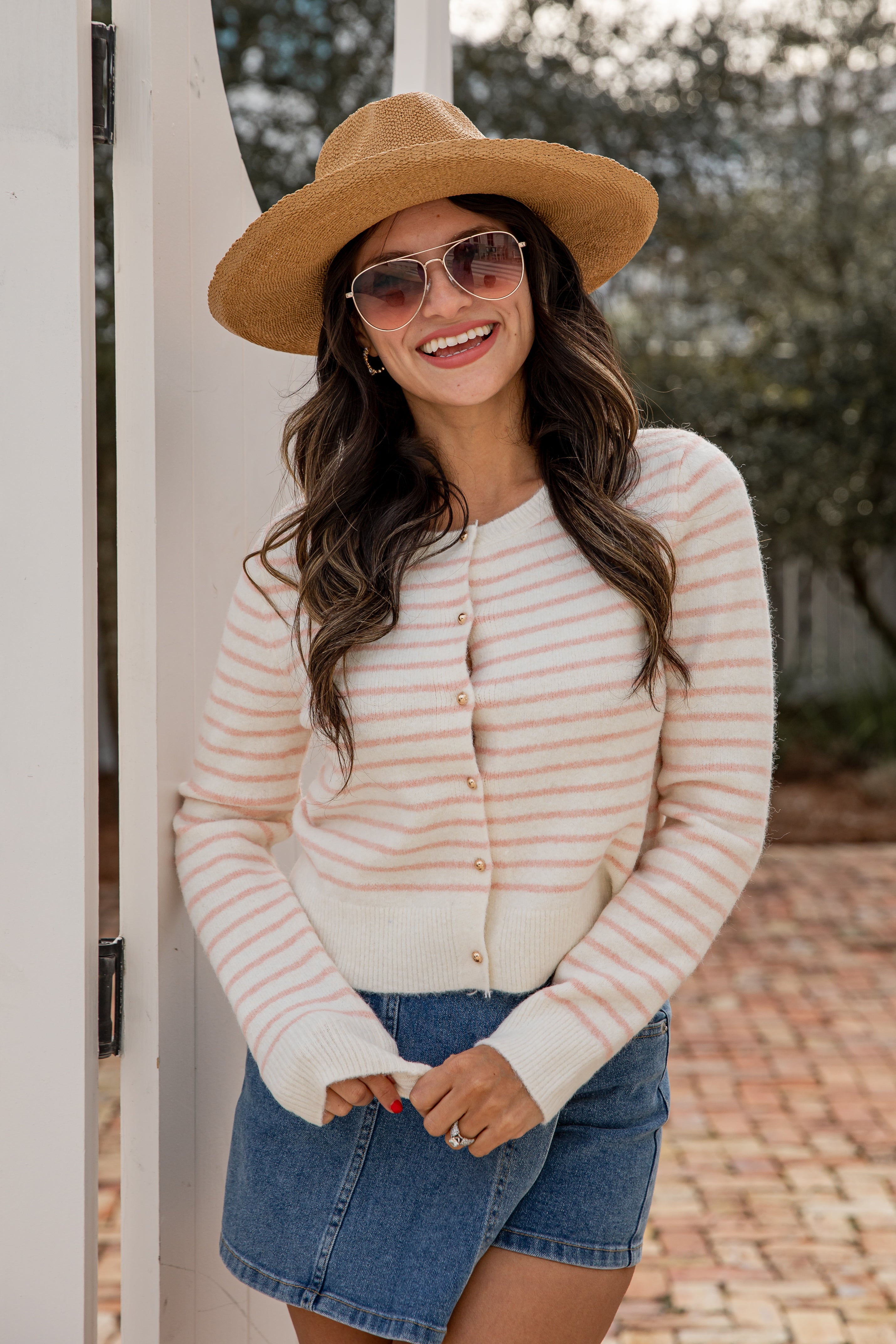 Woman wearing a striped sweater, denim shorts, and a hat outdoors.