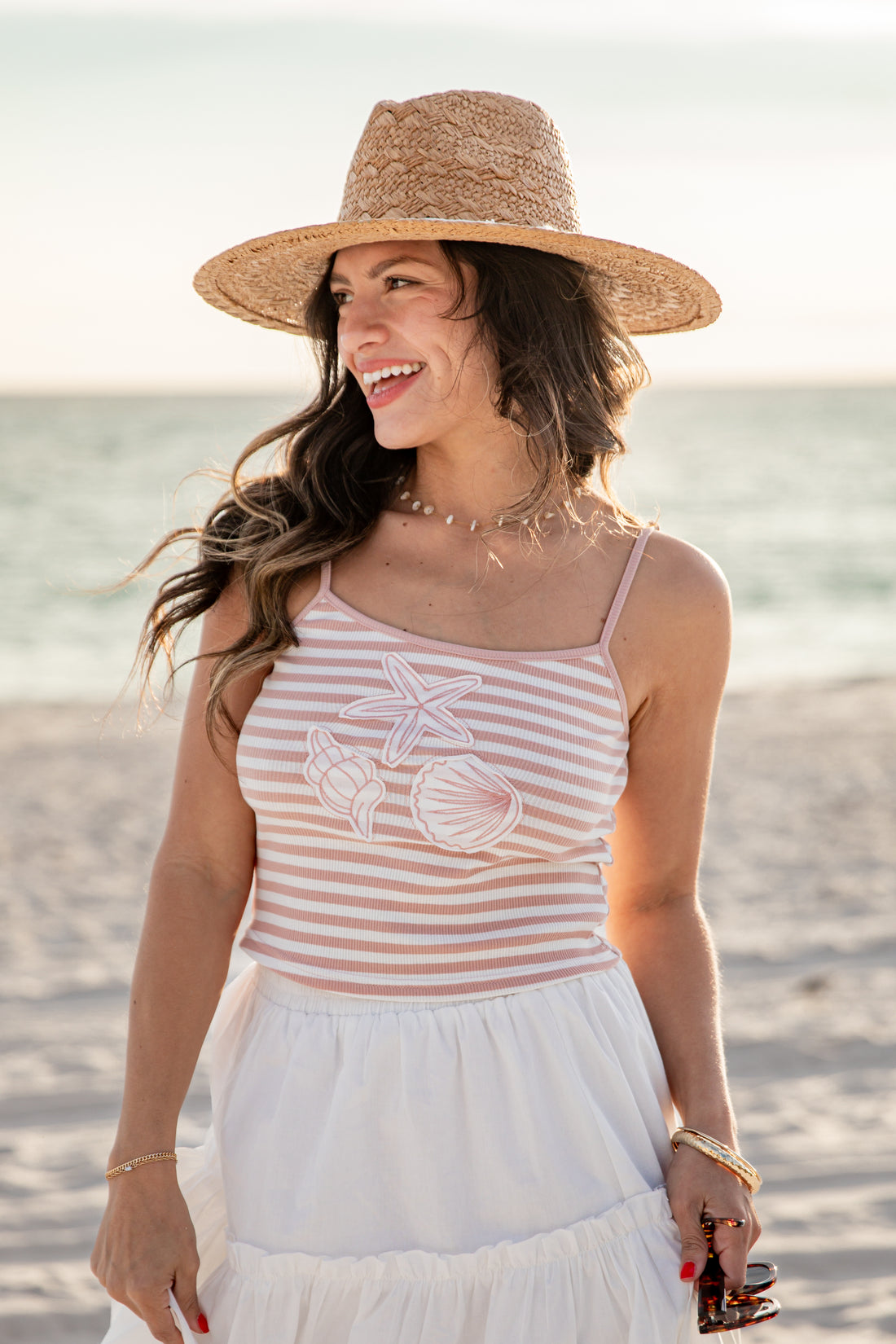Woman on a beach wearing a striped tank top and wide-brimmed hat.